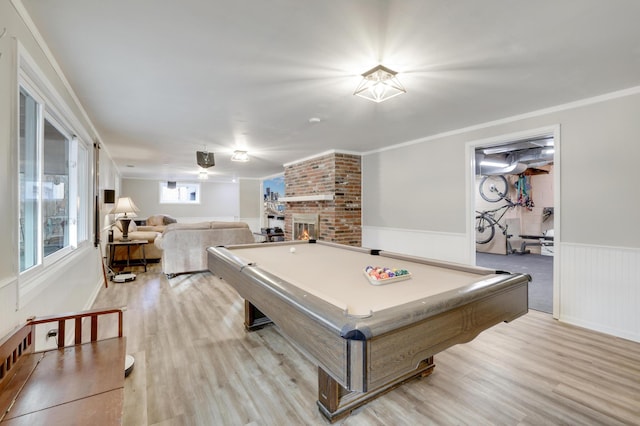 game room featuring billiards, a wainscoted wall, light wood-style flooring, ornamental molding, and a brick fireplace