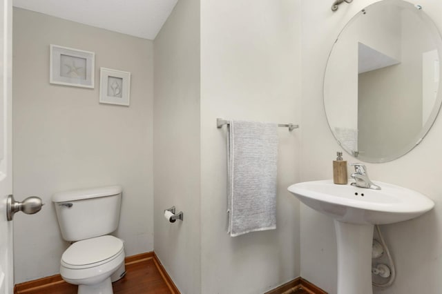 half bath with a sink, wood finished floors, toilet, and baseboards