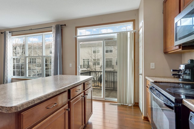 kitchen featuring plenty of natural light, stainless steel microwave, brown cabinetry, and wood finished floors