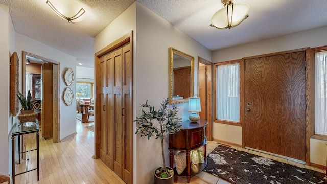 foyer entrance with baseboards, a textured ceiling, and light wood-style floors