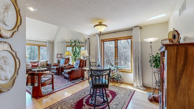 sitting room with a textured ceiling, light wood-type flooring, visible vents, and lofted ceiling