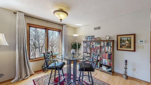 dining room with baseboards, light wood-style flooring, visible vents, and a textured ceiling