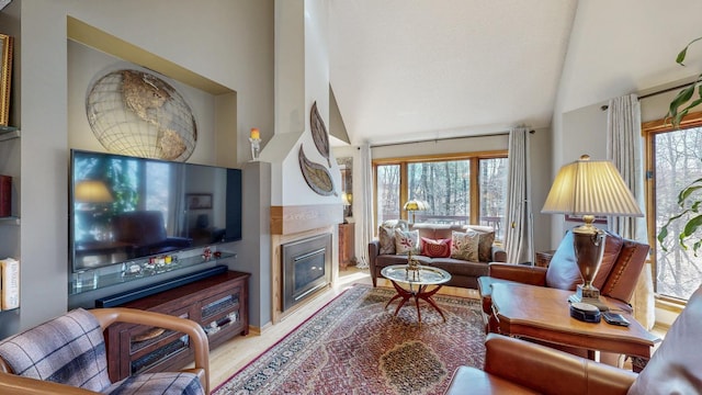 living area featuring a glass covered fireplace, vaulted ceiling, and wood finished floors