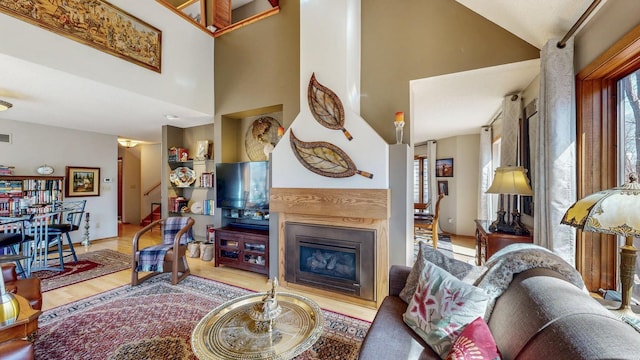 living room featuring a glass covered fireplace, wood finished floors, visible vents, and a high ceiling