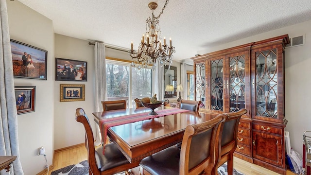 dining space with an inviting chandelier, a textured ceiling, visible vents, and light wood-style flooring
