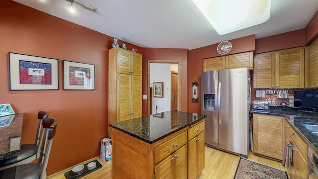 kitchen with stainless steel fridge with ice dispenser, light wood-type flooring, a kitchen island, dark stone counters, and brown cabinetry