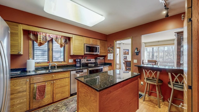 kitchen with a sink, brown cabinets, light wood-style floors, stainless steel appliances, and a kitchen island