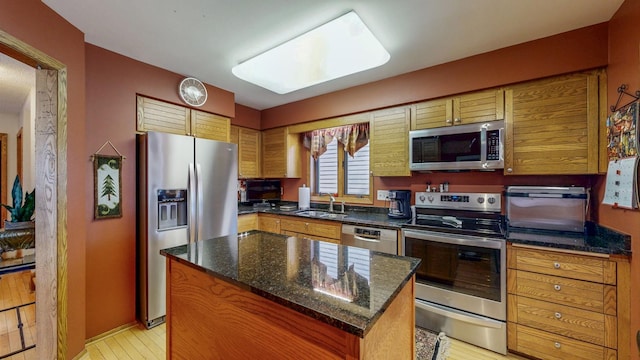 kitchen featuring stainless steel appliances, dark stone countertops, a sink, a center island, and brown cabinetry