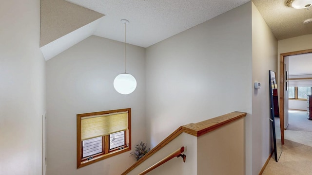 hallway with lofted ceiling, a textured ceiling, light colored carpet, and an upstairs landing