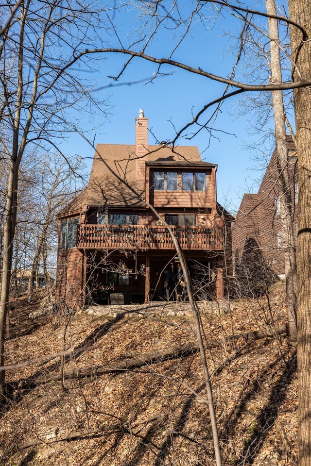 back of property featuring a wooden deck, a chimney, and roof with shingles