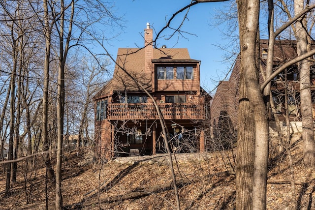 back of house featuring a chimney, a wooden deck, and a shingled roof