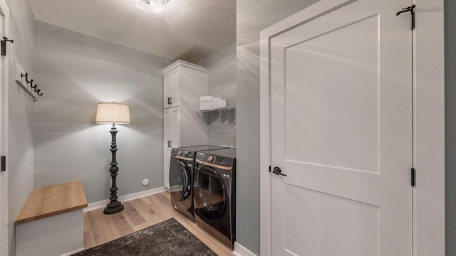 laundry room featuring washer and dryer, cabinet space, a textured ceiling, light wood-type flooring, and baseboards