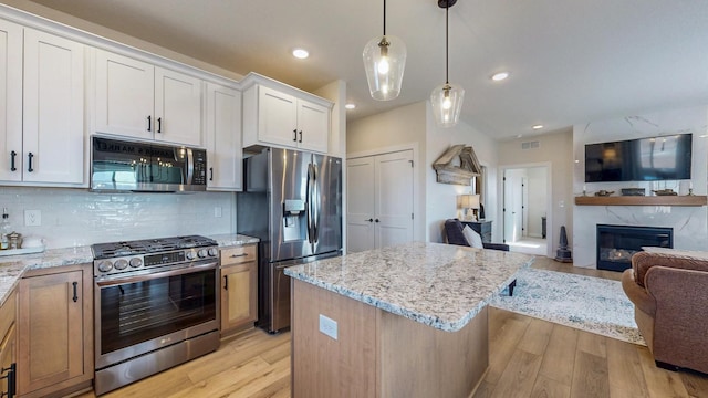 kitchen featuring light stone counters, a premium fireplace, appliances with stainless steel finishes, open floor plan, and light wood-type flooring