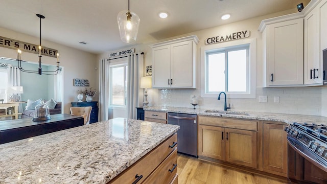 kitchen featuring gas range oven, stainless steel dishwasher, light wood-style floors, white cabinetry, and a sink