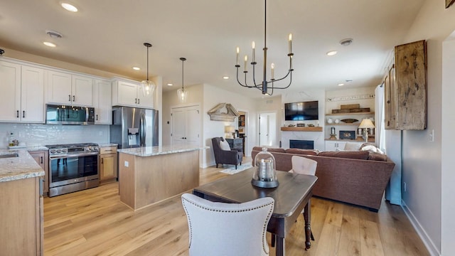 kitchen featuring stainless steel appliances, a fireplace, light wood-style floors, open floor plan, and a center island