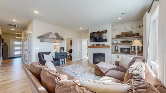 living area with recessed lighting, visible vents, light wood finished floors, and a premium fireplace