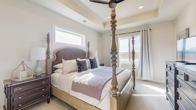 bedroom with light carpet, a tray ceiling, a ceiling fan, and baseboards