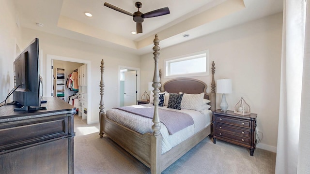 bedroom featuring light colored carpet, baseboards, a spacious closet, a closet, and a raised ceiling