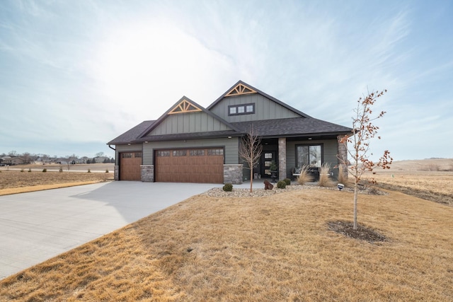 craftsman house with an attached garage, board and batten siding, a front yard, stone siding, and driveway