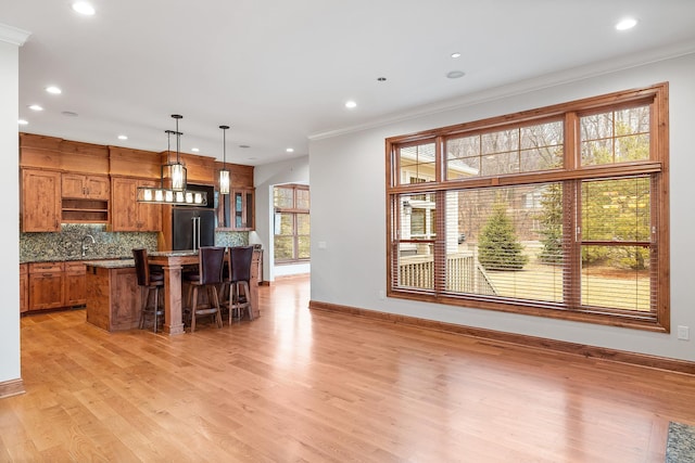 kitchen featuring light wood finished floors, decorative backsplash, brown cabinetry, a center island, and high end fridge