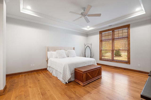 bedroom with light wood-style floors, a tray ceiling, ornamental molding, and baseboards