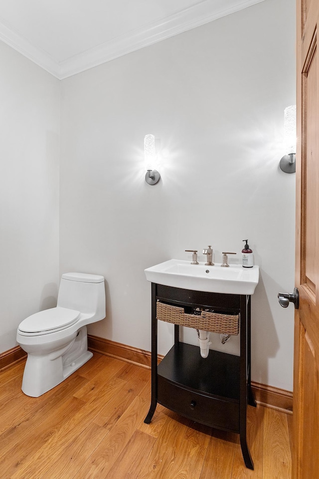 half bath featuring ornamental molding, wood finished floors, toilet, and baseboards