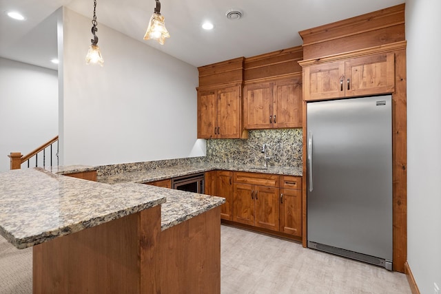 kitchen with a peninsula, brown cabinetry, built in fridge, and visible vents