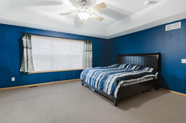 carpeted bedroom featuring a tray ceiling, baseboards, visible vents, and ceiling fan