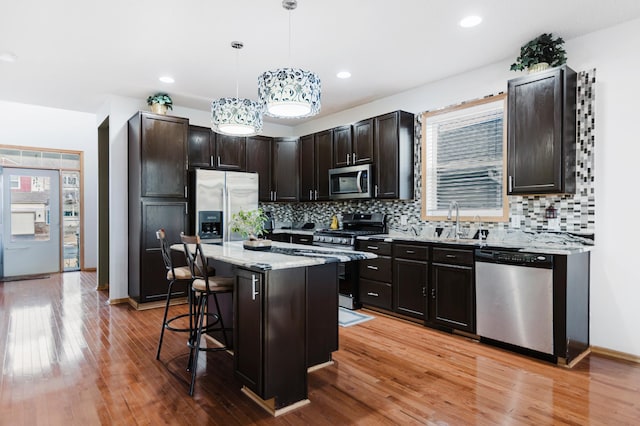 kitchen with light wood finished floors, a sink, hanging light fixtures, appliances with stainless steel finishes, and a kitchen bar