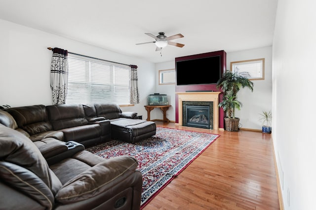 living room featuring a fireplace with flush hearth, baseboards, light wood-type flooring, and a ceiling fan