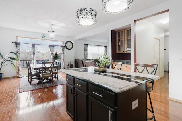 kitchen with pendant lighting, a kitchen island, light wood-style floors, a breakfast bar area, and light stone countertops