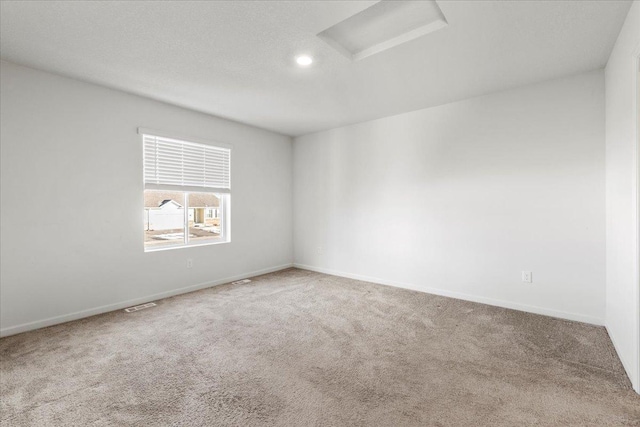 unfurnished room with a textured ceiling, carpet flooring, visible vents, baseboards, and attic access