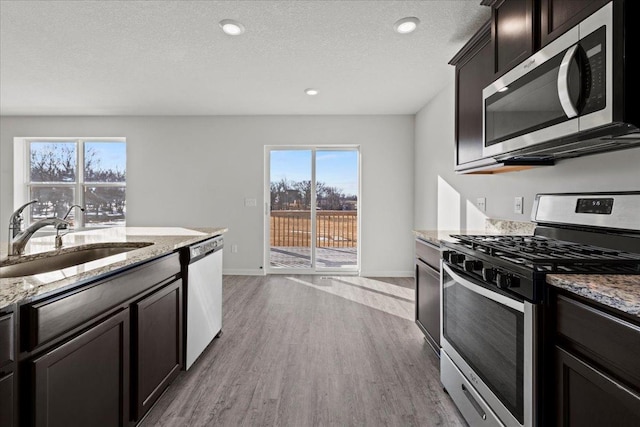 kitchen with light stone countertops, appliances with stainless steel finishes, a sink, and wood finished floors