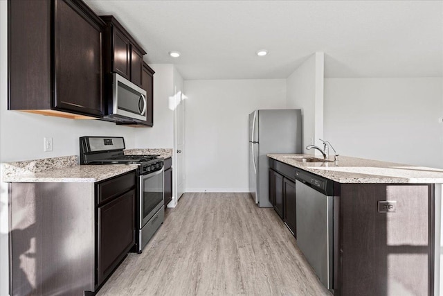 kitchen with stainless steel appliances, dark brown cabinets, a sink, and light wood-style floors