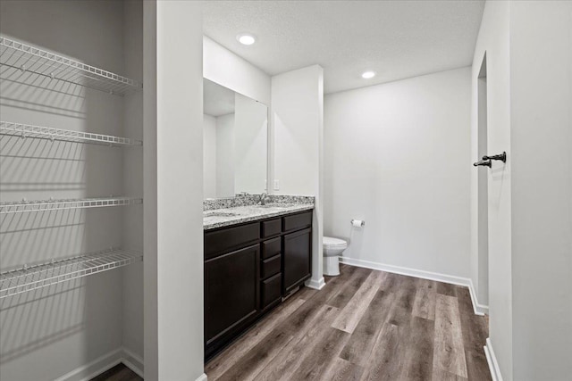 bathroom with toilet, recessed lighting, wood finished floors, baseboards, and double vanity