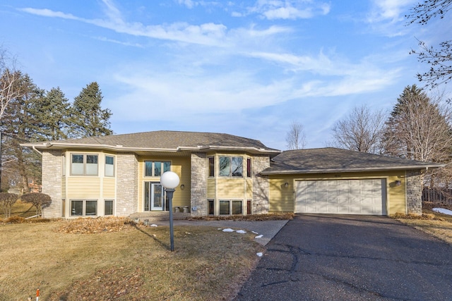 view of front facade with a front yard, a shingled roof, a garage, stone siding, and aphalt driveway