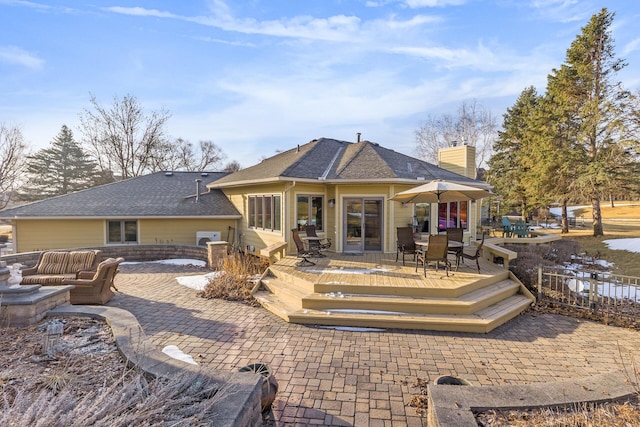 rear view of property with a chimney, an outdoor living space, a wooden deck, and a shingled roof