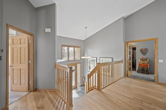 hall with baseboards, an upstairs landing, high vaulted ceiling, and wood finished floors