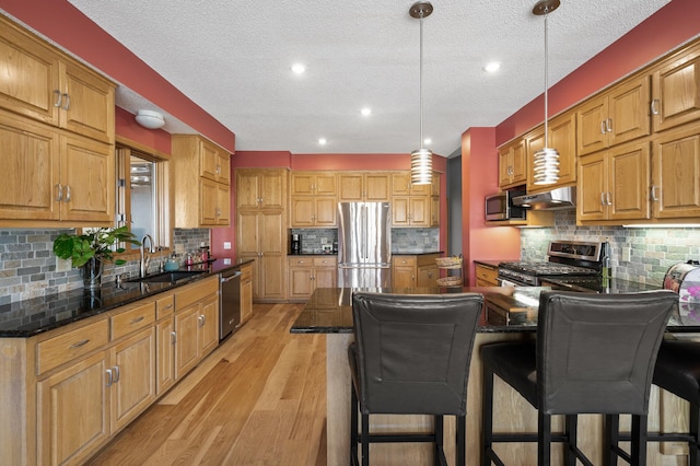 kitchen with a peninsula, light wood-style flooring, a sink, under cabinet range hood, and appliances with stainless steel finishes