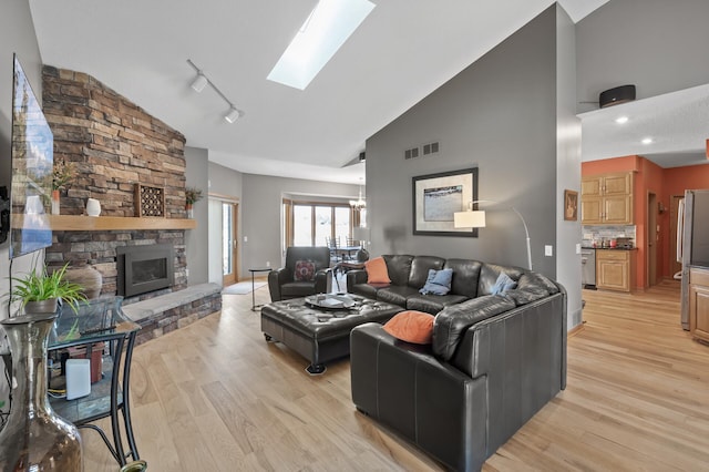 living area featuring visible vents, high vaulted ceiling, a stone fireplace, a skylight, and light wood finished floors