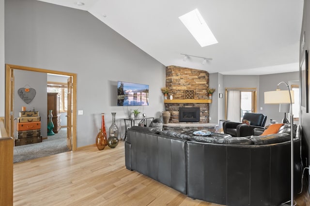 living area with light wood-type flooring, a stone fireplace, rail lighting, a skylight, and high vaulted ceiling