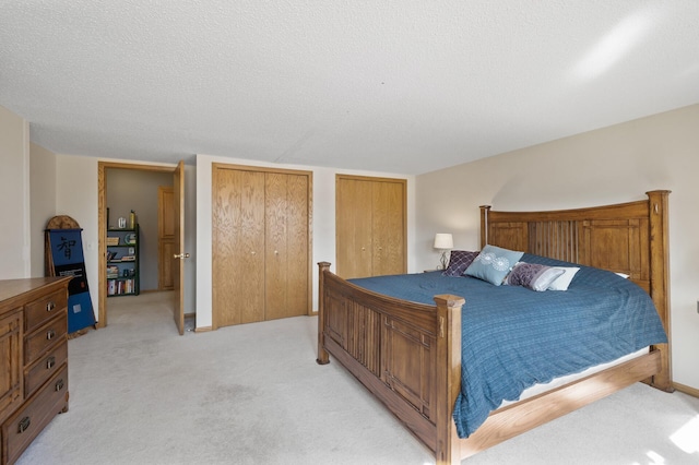 bedroom with light colored carpet, multiple closets, a textured ceiling, and baseboards