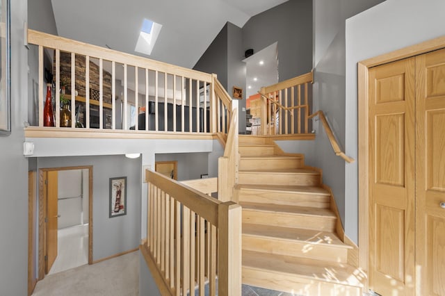 stairway with high vaulted ceiling, a skylight, baseboards, and carpet floors