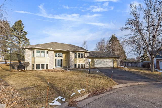 view of front of property featuring driveway, stone siding, fence, an attached garage, and a front yard