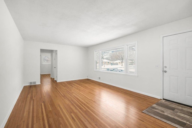 unfurnished living room featuring baseboards, visible vents, and wood finished floors