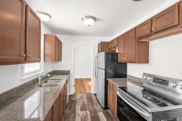 kitchen with dark wood-style floors, appliances with stainless steel finishes, brown cabinets, stone counters, and a sink