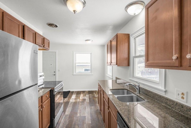 kitchen featuring visible vents, electric range, brown cabinetry, freestanding refrigerator, and a sink