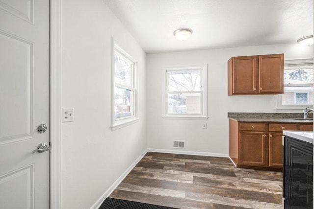 kitchen with dark wood-style flooring, brown cabinets, visible vents, a sink, and baseboards