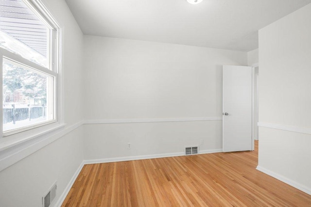 empty room with wood finished floors, visible vents, and baseboards