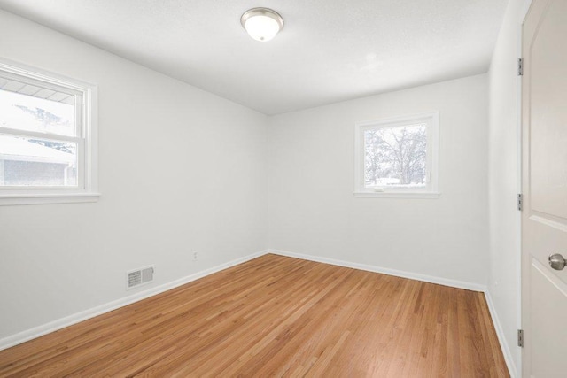 empty room with light wood-type flooring, visible vents, and baseboards